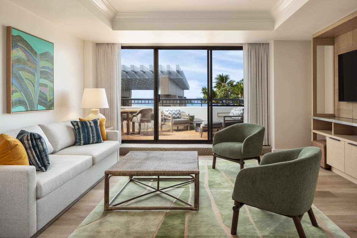 Un salon moderne comprenant un canapé, des fauteuils, une table basse, un téléviseur et un balcon aménagé avec du mobilier d’extérieur.