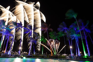 Vista noturna de um resort com palmeiras e piscina.