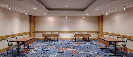 A conference room with a carpeted floor, two tables with chairs, and recessed ceiling lighting.