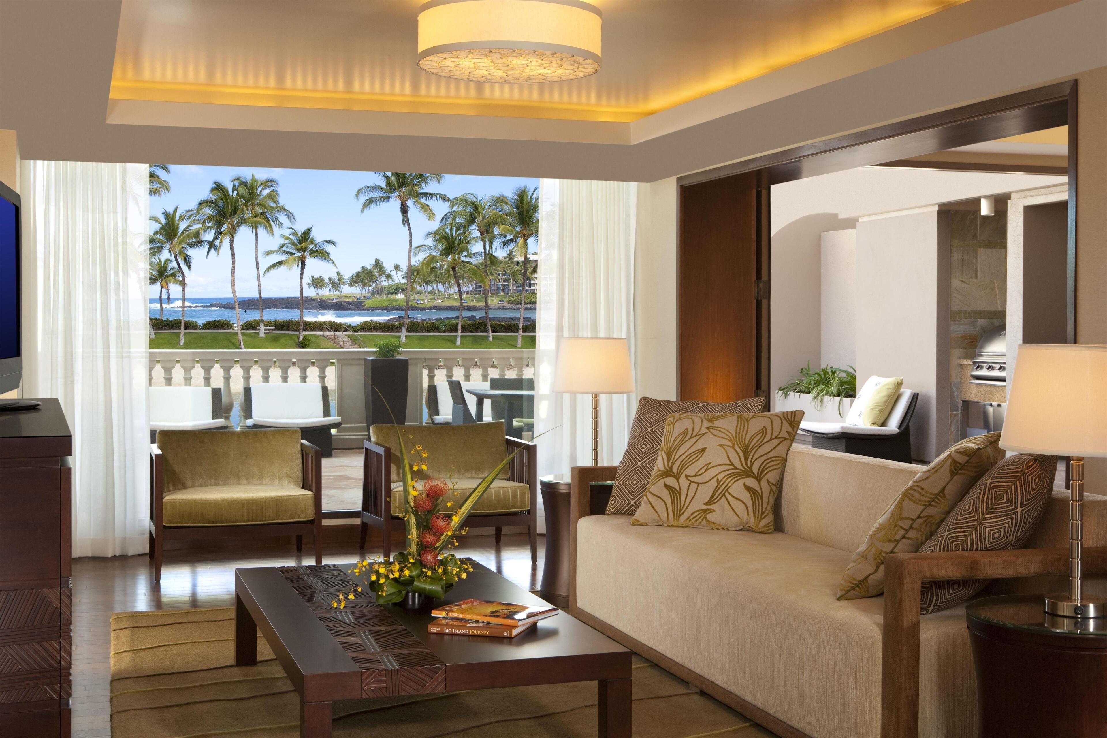 A hotel room with a balcony, a sofa, a coffee table, and a TV.