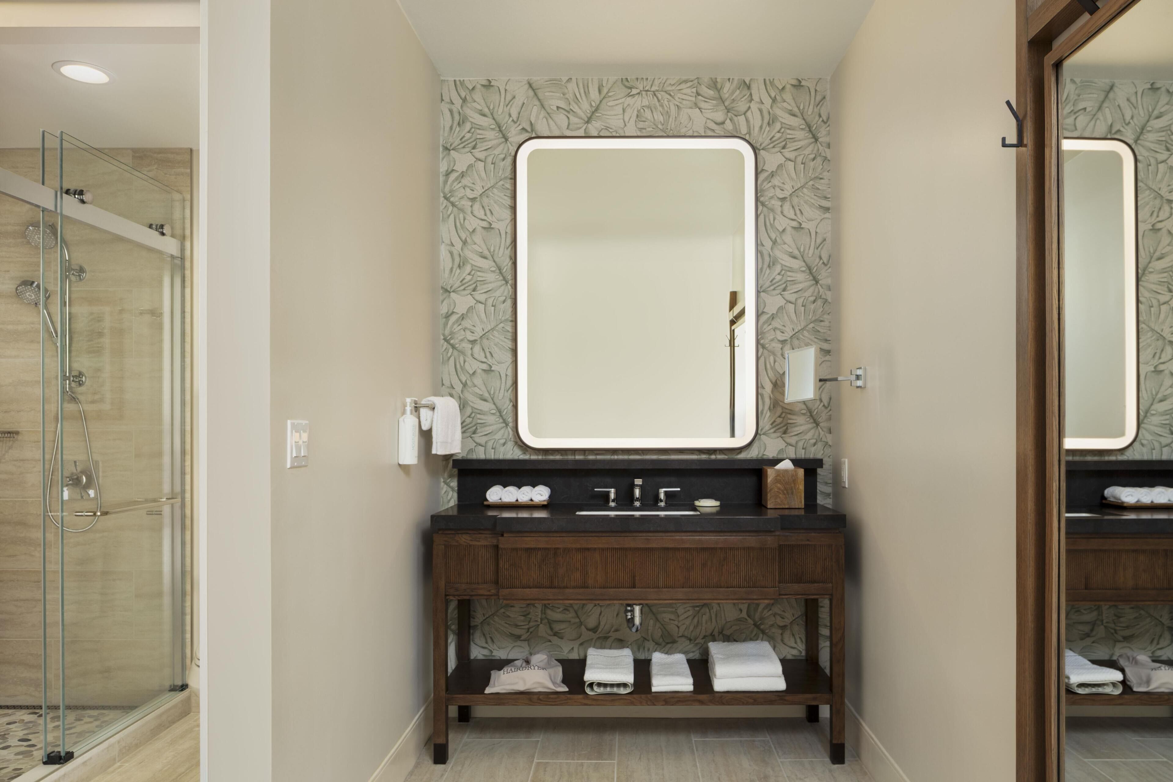 A bathroom with a glass-enclosed shower, a large mirror, and a vanity with a towel rack.