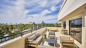 Ein Balkon mit einer Couch, Stühlen, einem Tisch und Blick auf Palmen und Gebäude.