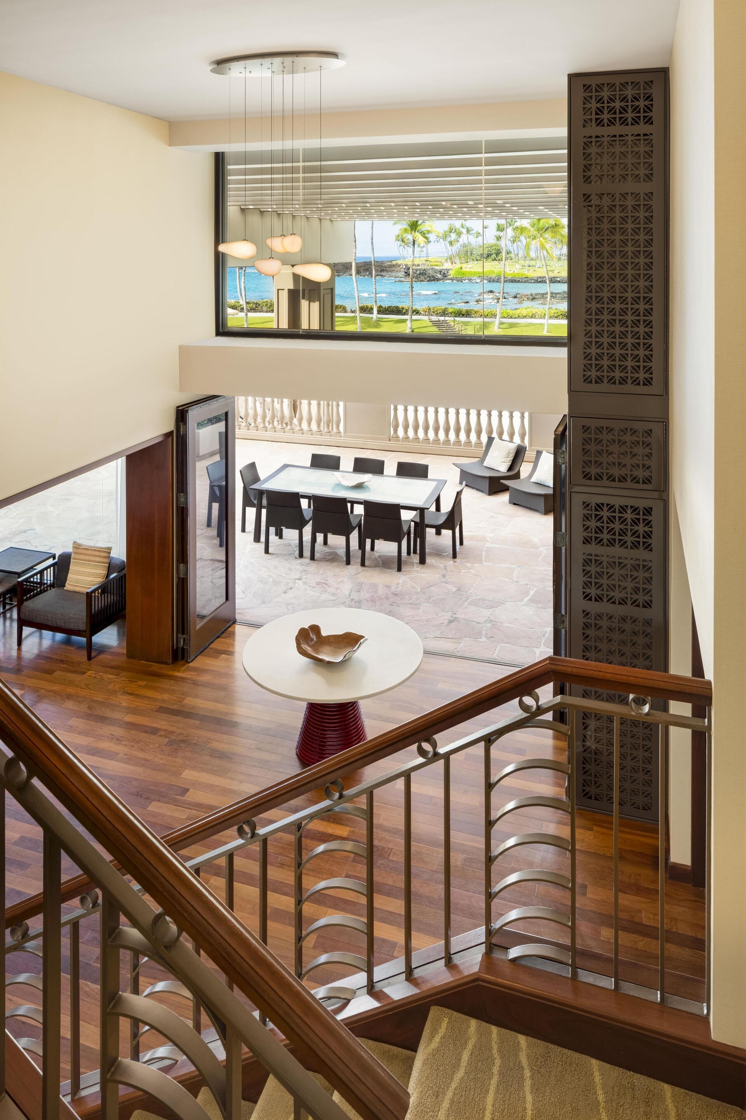 A spacious room with a large window overlooking a scenic view, a dining area with a table and chairs, and a staircase with a railing.