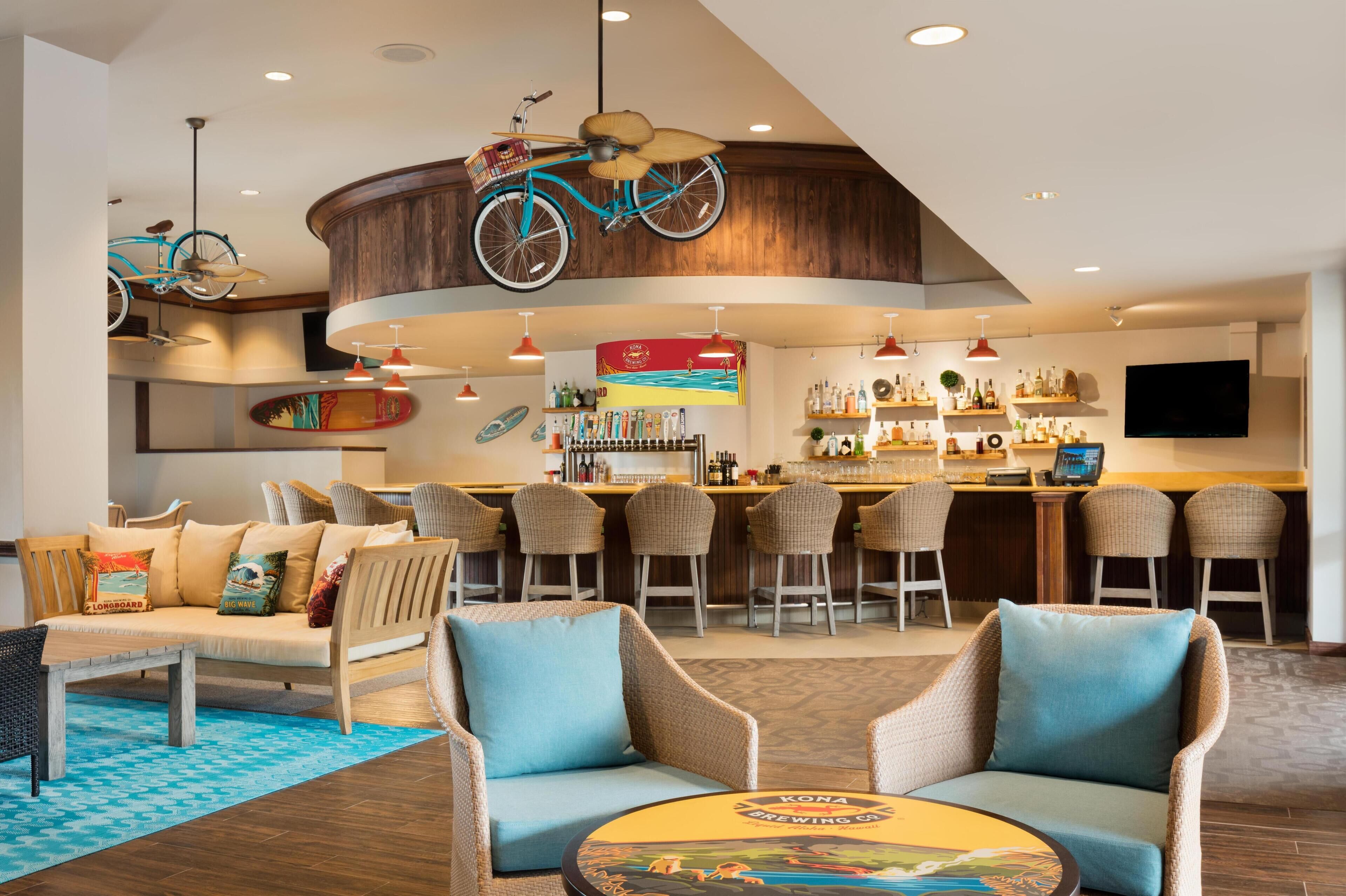 A bar area with wicker chairs, a round table with a coaster, and a ceiling-mounted bicycle.