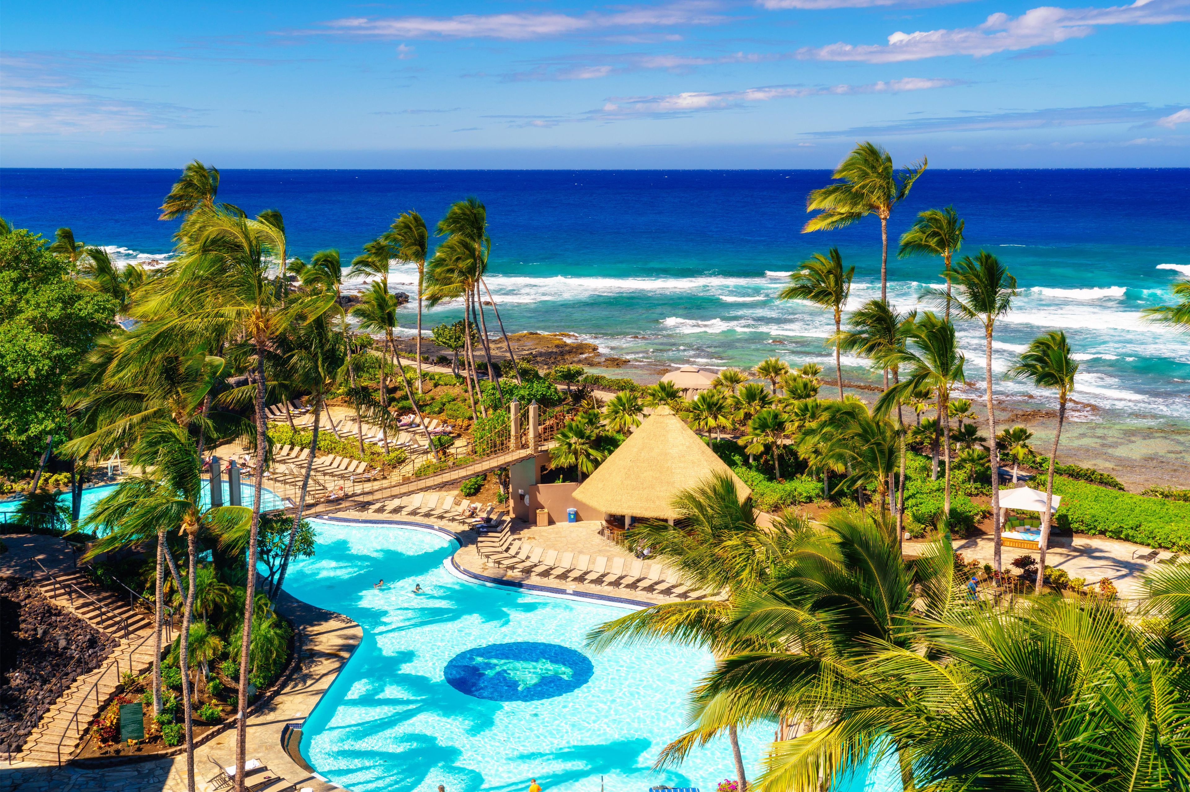 A resort with a swimming pool, palm trees, and a view of the ocean.