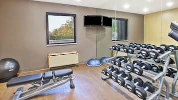 A gym with exercise equipment, a bench, a mirrored wall, and a window with a view of trees.