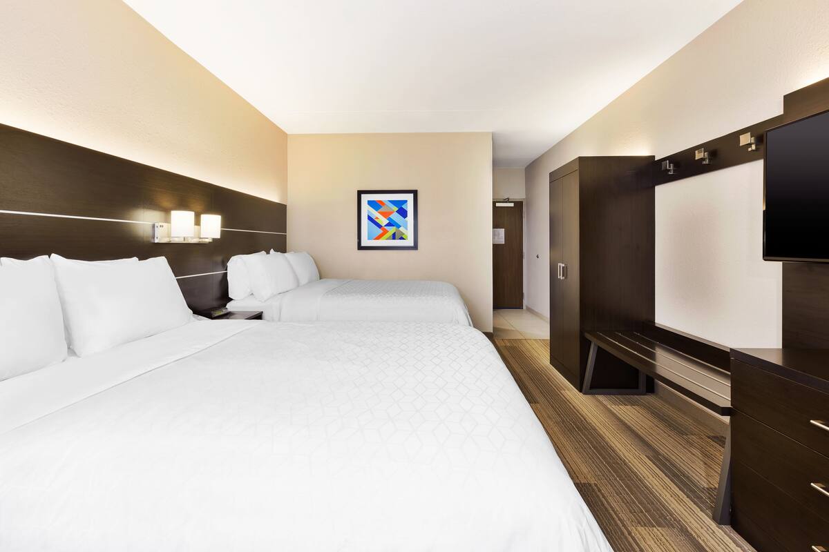 A hotel room with two beds, a flat-screen TV, a painting on the wall, and a wooden floor.
