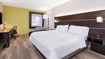 A hotel room with a large bed, a desk, a chair, a nightstand, and a wall-mounted lamp.