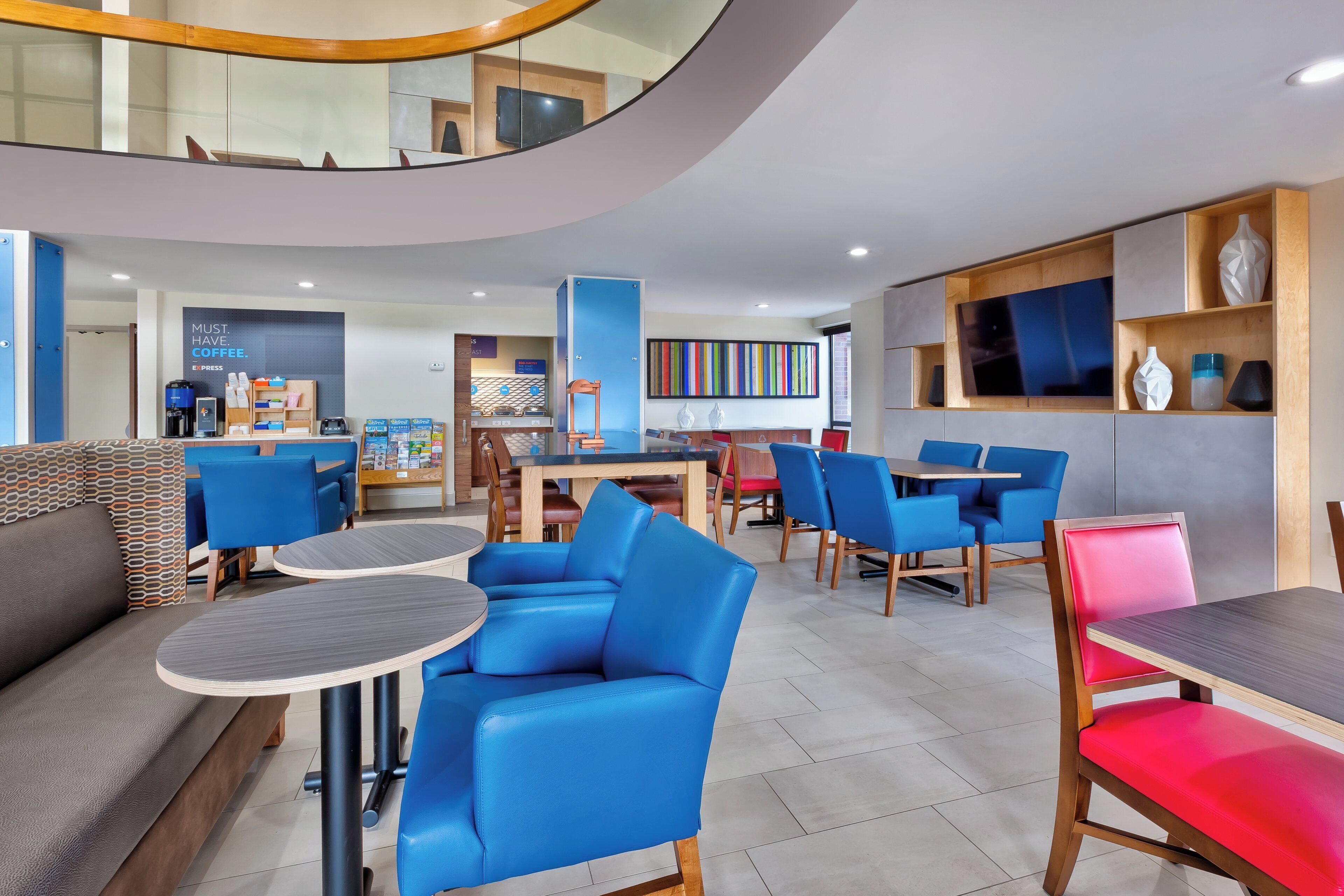 A modern hotel lobby with seating areas, a coffee station, and a TV mounted on the wall.