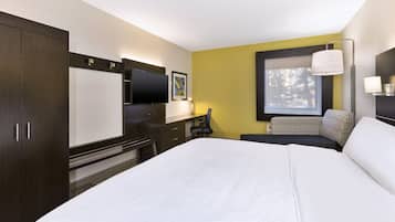 A hotel room with a large bed, a desk with a chair, a TV, and a window with a view of trees.