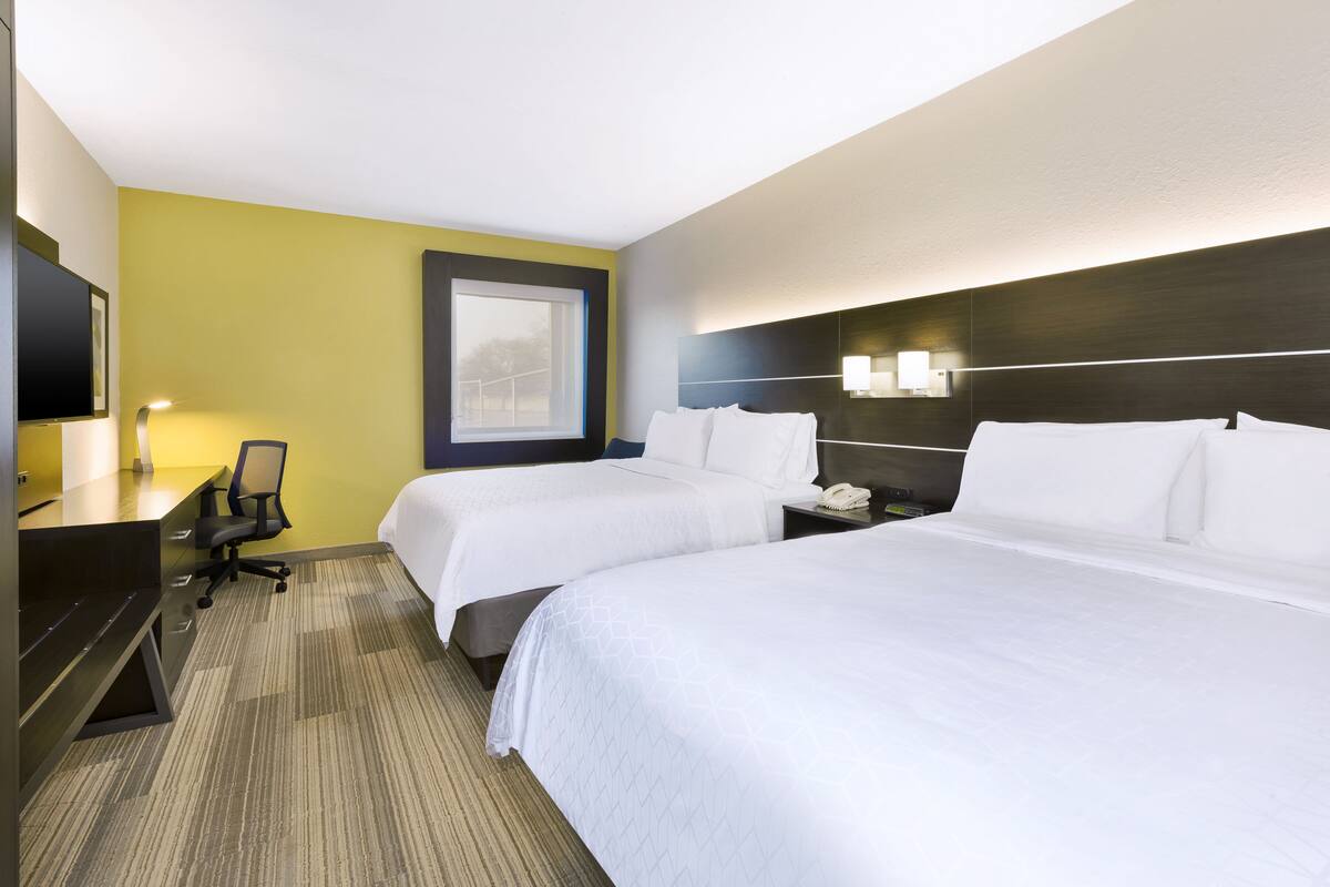 A hotel room with two beds, a desk with a chair, a TV, and a window with a view.