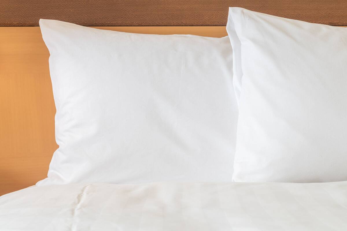 A bed with white bedding and pillows against a wooden headboard.