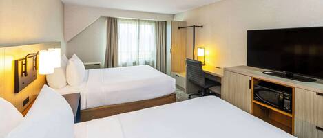 A hotel room with two beds, a desk with a computer, a TV, and a microwave.