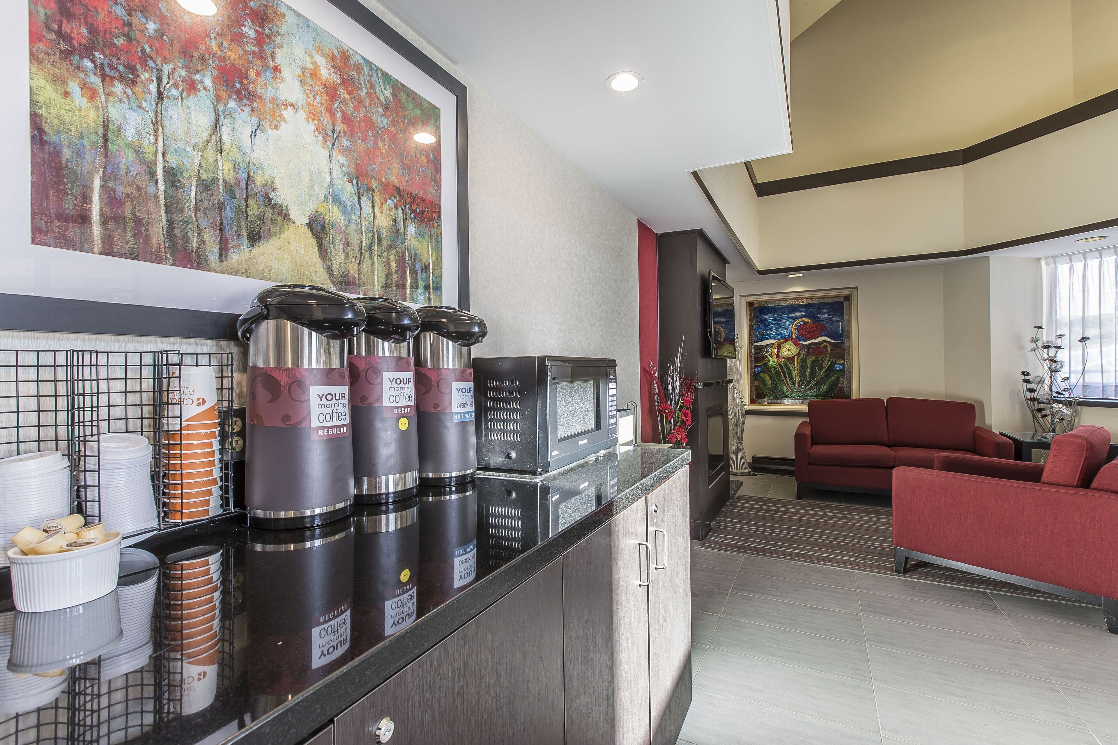 A modern kitchen with coffee dispensers, a microwave, and a red sofa in the living area.