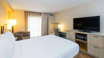 A hotel room with a large bed, a desk with a computer, a flat-screen TV, a microwave, and a chair.