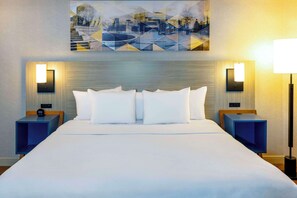 Una habitación de hotel con una cama grande, dos mesitas de noche, un cuadro colgado en la pared y dos lámparas de pared.