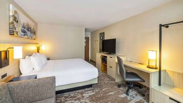 Habitación de hotel con cama, escritorio, silla, televisión y un cuadro en la pared.