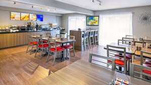 Un comedor moderno con suelo de madera, sillas rojas acolchadas y una isla central con una cafetera.