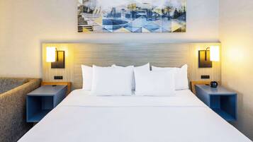 A hotel room with a large bed, two bedside tables, and a cityscape painting on the wall.
