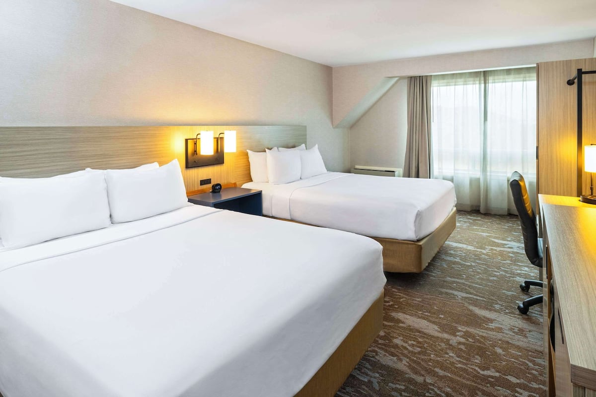A hotel room with two beds, a desk, and a chair.