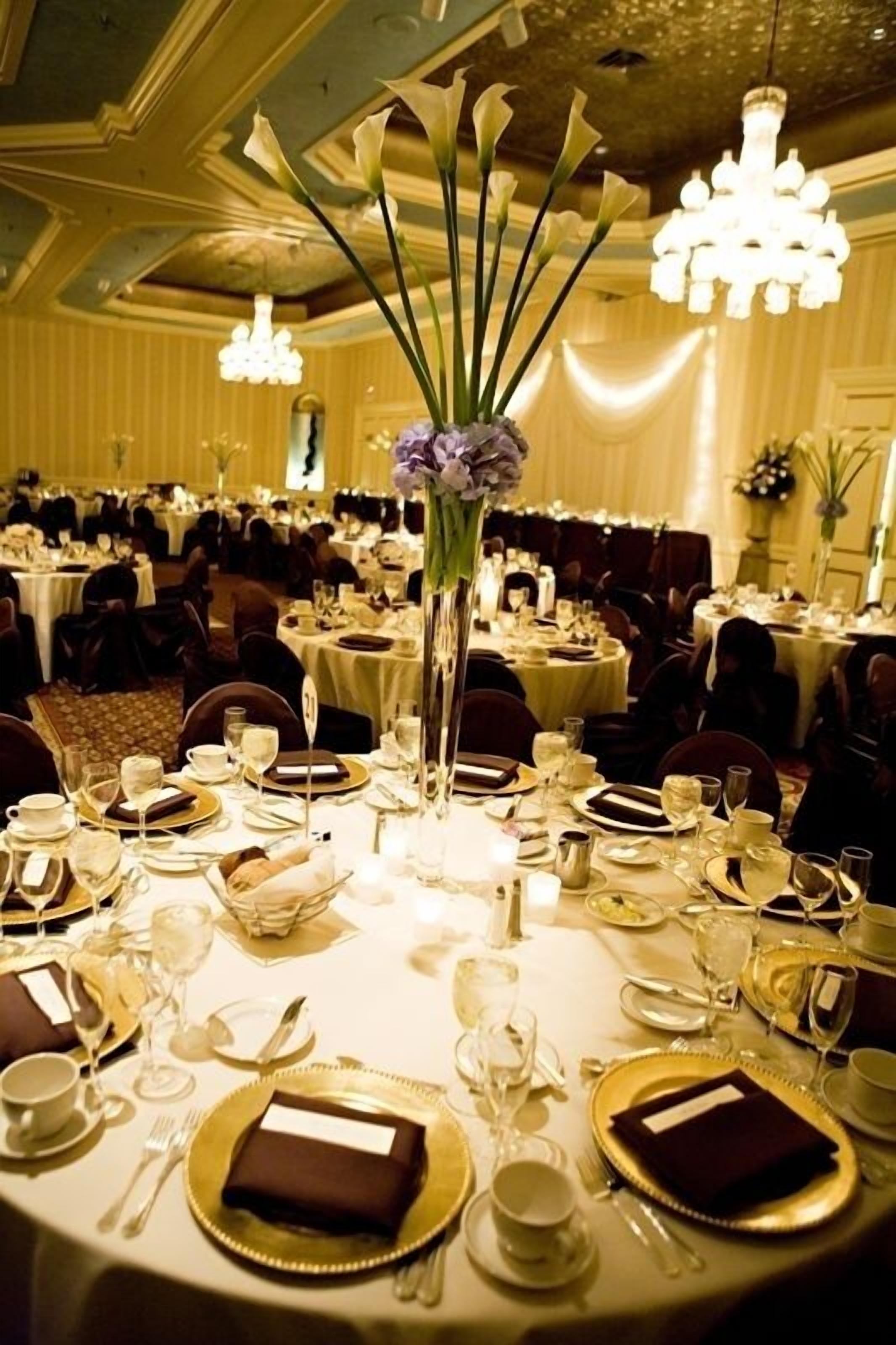 A banquet hall with round tables set for a formal event, featuring floral centerpieces and elegant table settings.