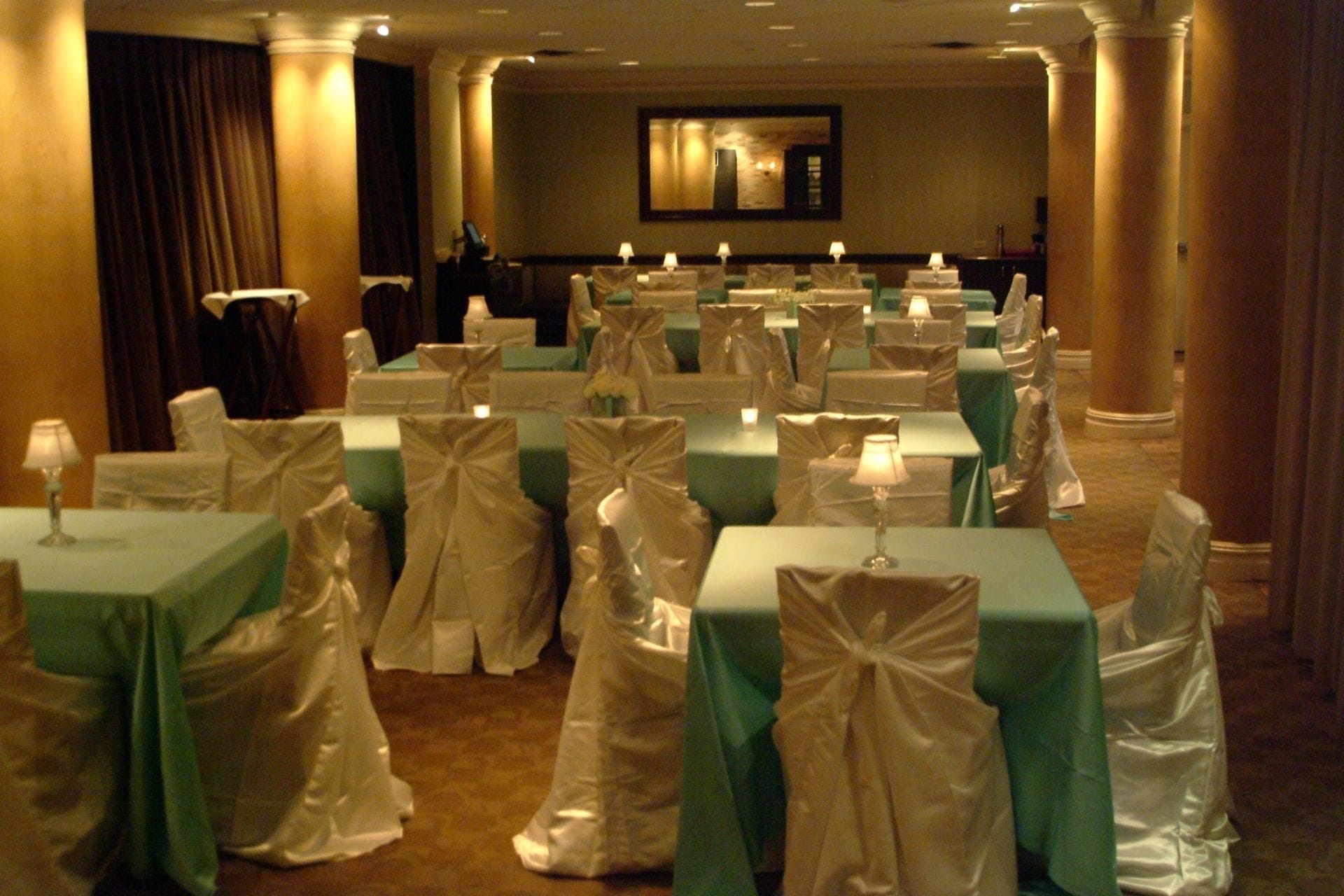 Une salle de banquet où les tables sont recouvertes de nappes blanches et les chaises sont ornées de rubans blancs, disposées en rangées.