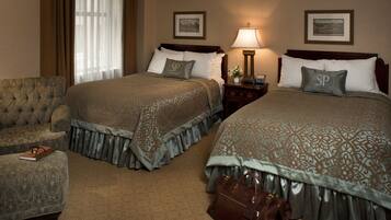 A hotel room with two beds, a nightstand with a lamp, a chair, and a suitcase.