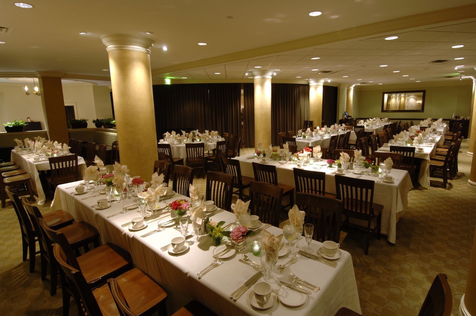 Un salón de banquetes con varias mesas dispuestas para comer, con manteles blancos y centros de mesa florales.