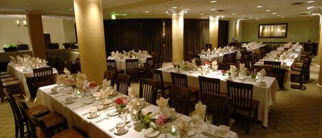 A banquet hall with multiple tables set for dining, featuring white tablecloths and floral centerpieces.
