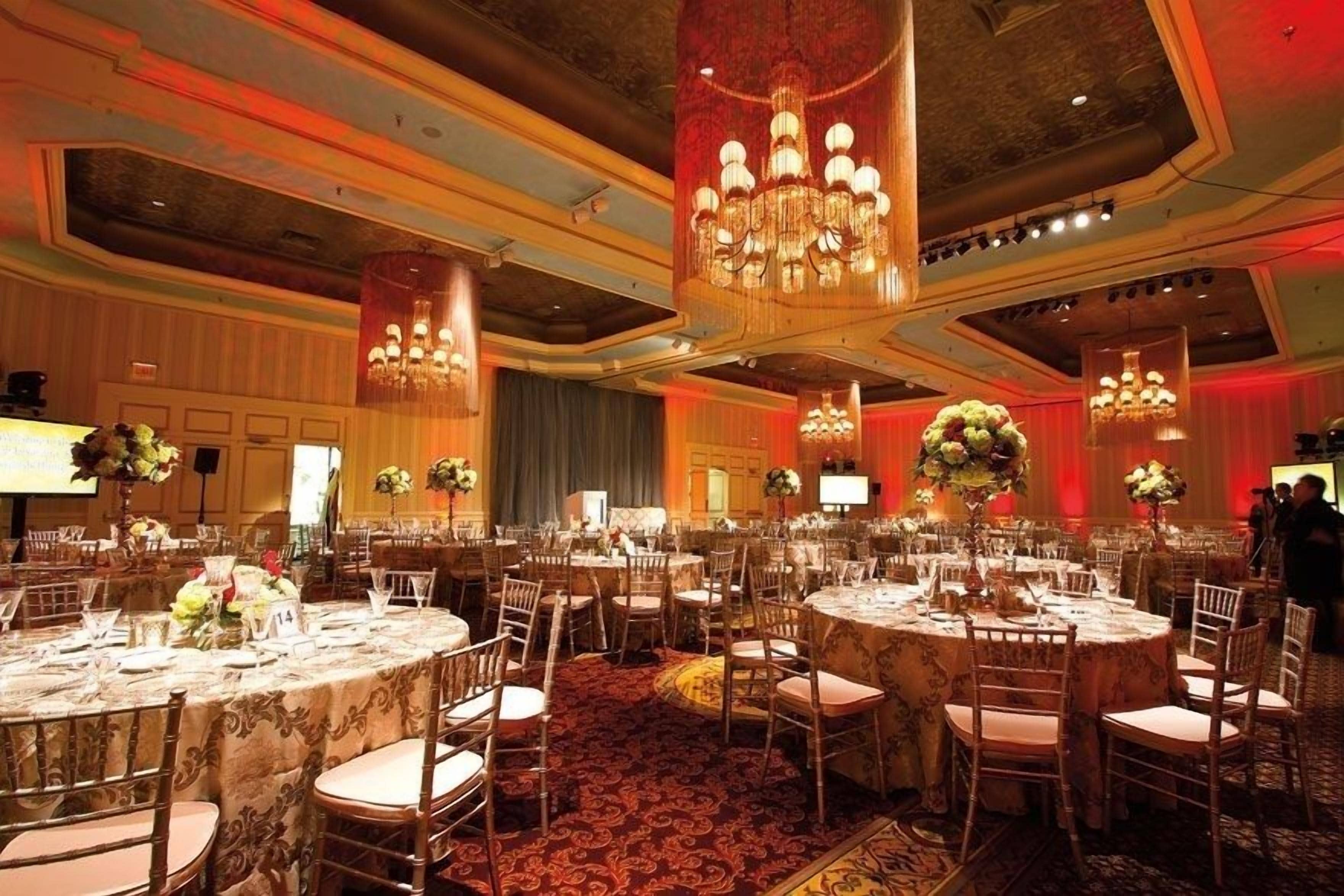 A banquet hall with round tables, chairs, and chandeliers.