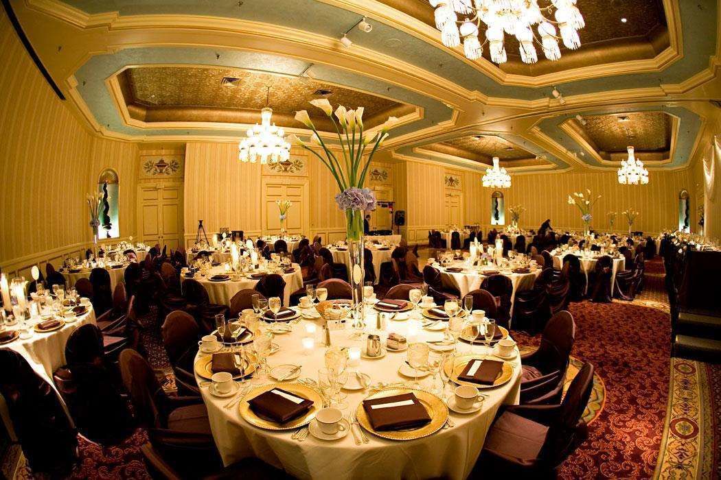 Une salle de banquet avec des tables rondes dressées pour le repas, des lustres et un sol recouvert de moquette.
