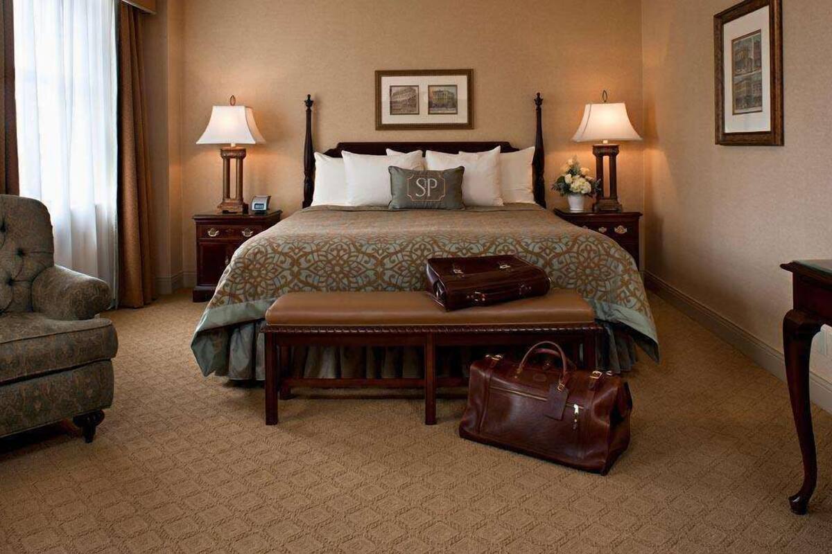 Ein Hotelzimmer mit einem großen Bett, zwei Nachttischen, einer Bank und einem Sessel.