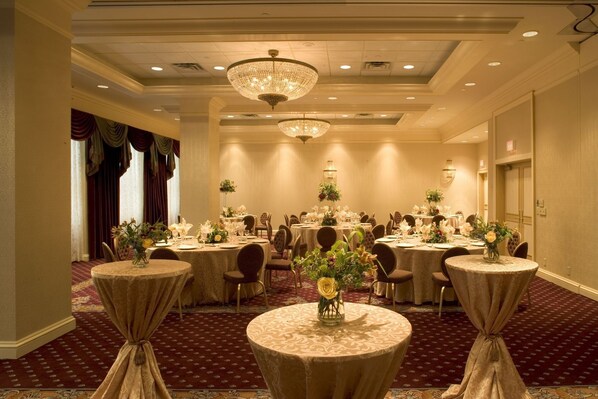 A banquet hall with round tables, chandeliers, and floral centerpieces.