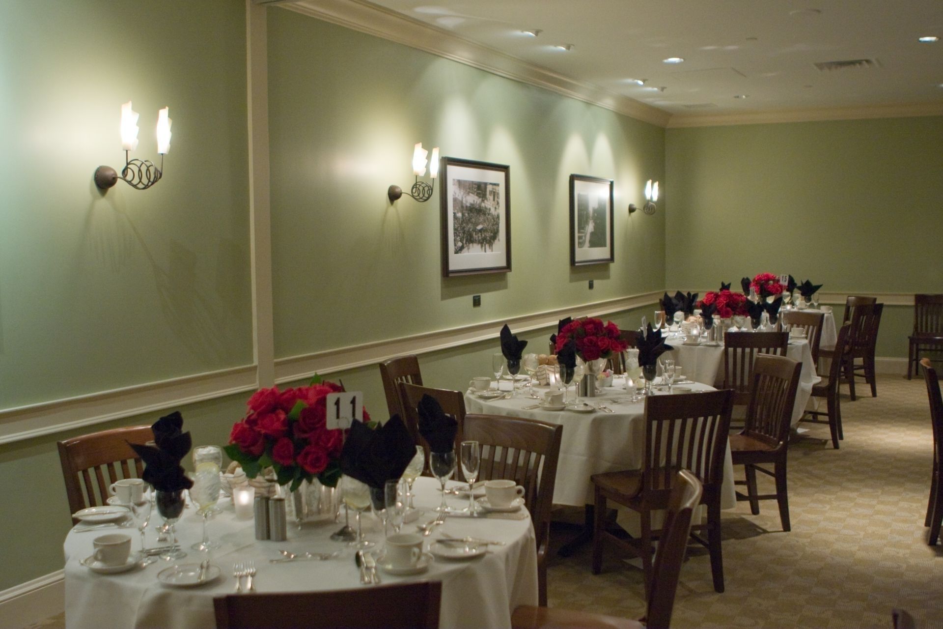 A dining area with tables set for service, framed pictures on the walls, and a carpeted floor.