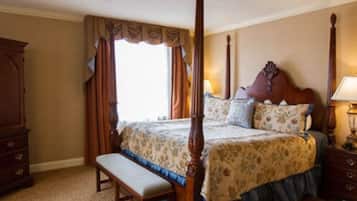 Un lit à baldaquin avec une couvre-lit à motifs floraux, un banc en bois et une table de chevet avec une lampe.