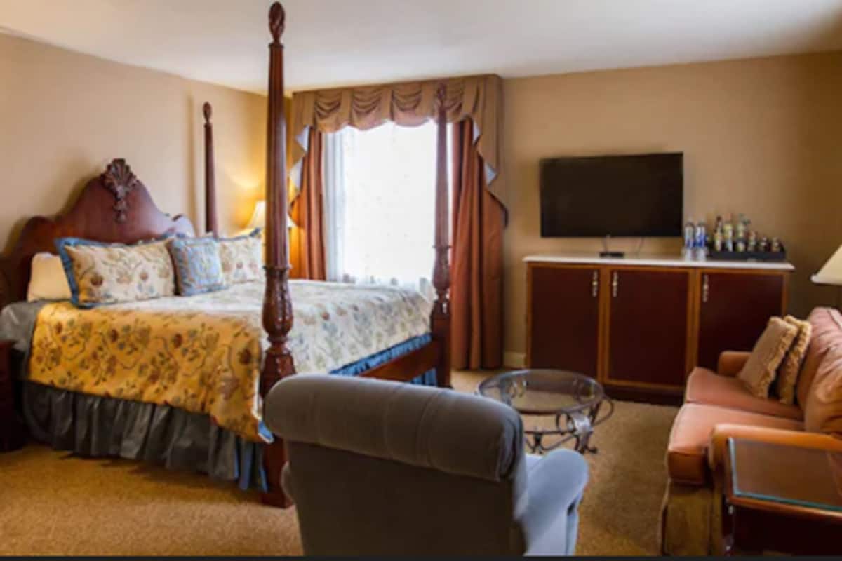 Ein Hotelzimmer mit einem Himmelbett, einem Fernseher, einer Couch und einem kleinen Tisch.