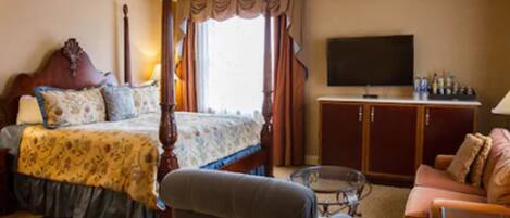 Habitación de hotel con cama con dosel, televisión, sofá y una pequeña mesa.
