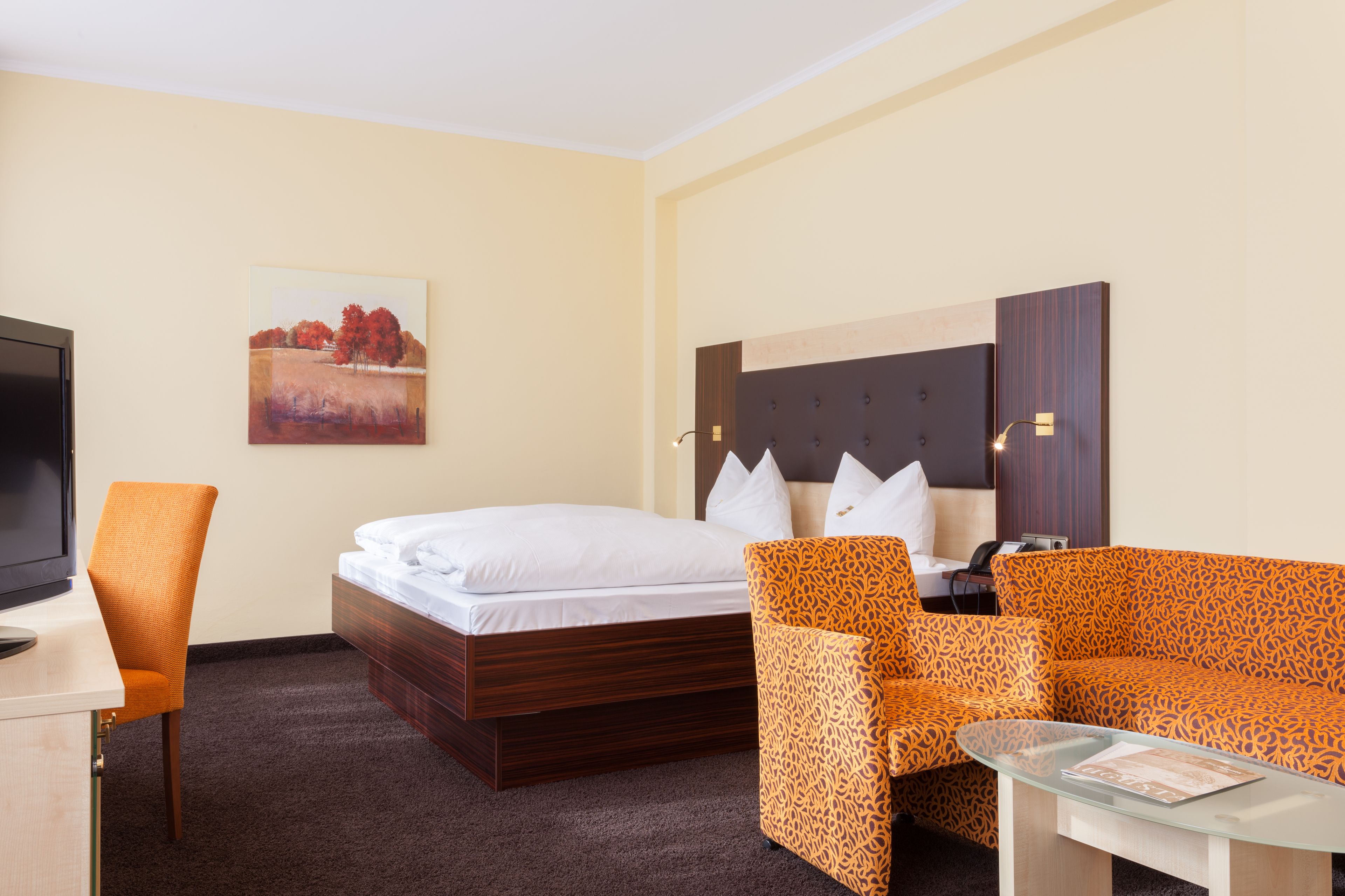 A hotel room with a bed, a sofa, a chair, a desk, and a television.