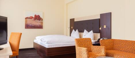 A hotel room with a bed, a sofa, a chair, a desk, and a television.