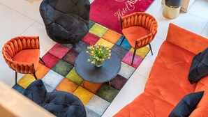 A hotel lobby with a colorful checkered carpet, a round table with a vase of flowers, and orange and black upholstered chairs. - Best Western Hotel Augusta (Augsburg)