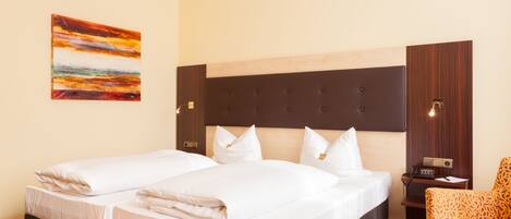A hotel room with two beds, a wooden headboard, a small table, a chair, and a painting on the wall.