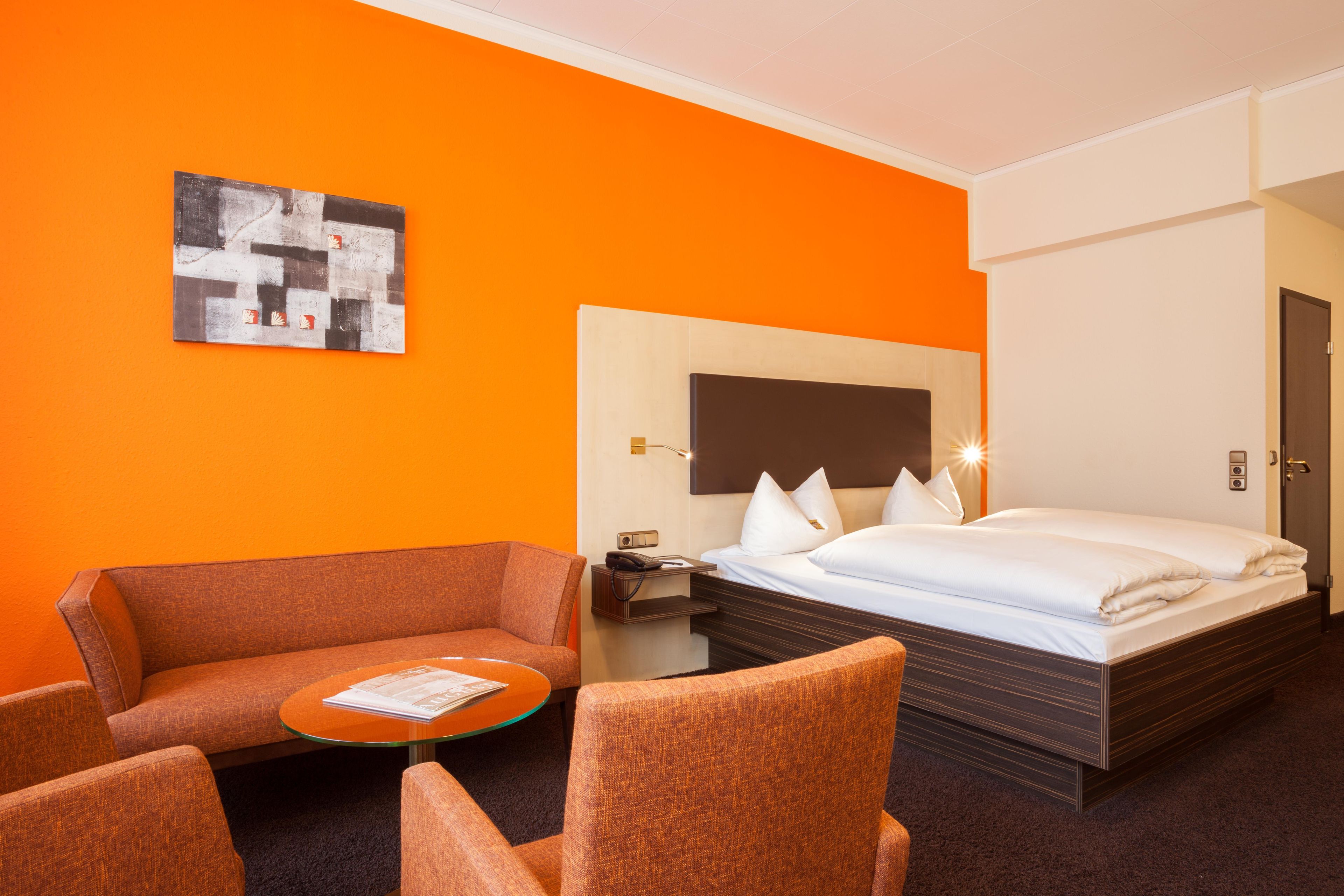 Una habitación de hotel con cama, sofá, una mesita y un cuadro en la pared.