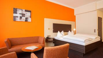 Una habitación de hotel con cama, sofá, una mesita y un cuadro en la pared.
