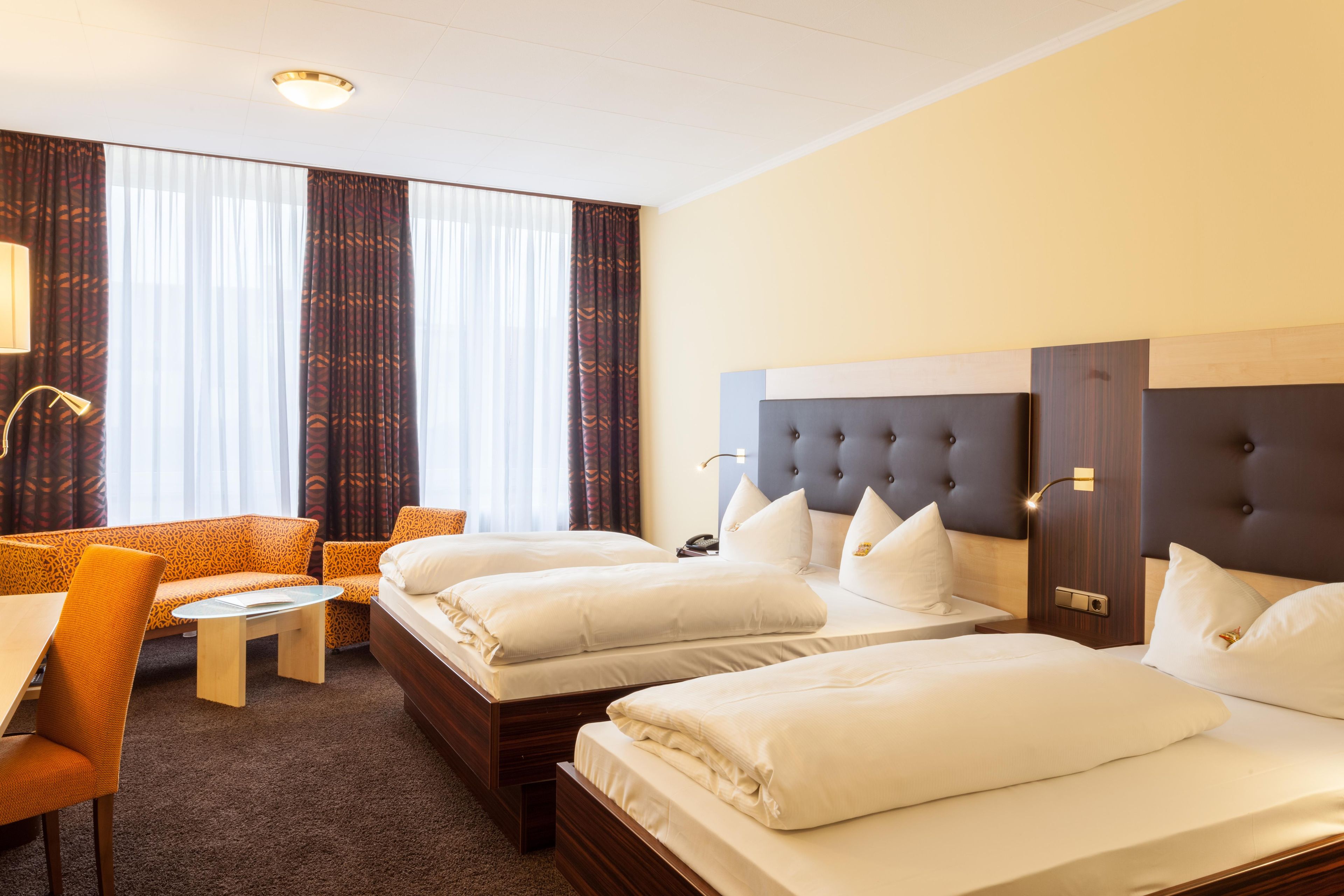 Una habitación de hotel con dos camas, un sofá, una mesita y una lámpara.