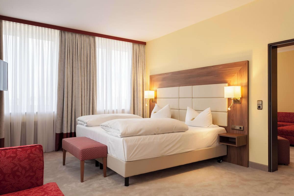 Ein Hotelzimmer mit einem großen Bett, zwei Nachttischen mit Lampen, einem roten Sessel und einer roten Couch.