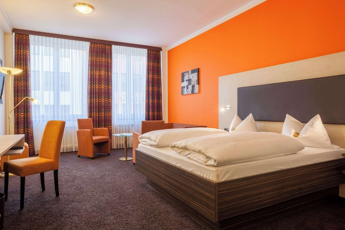 Ein Hotelzimmer mit einem großen Bett, zwei Sesseln, einem Schreibtisch und einem kleinen Tisch.