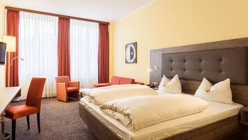 Una camera d'albergo con un letto grande, due poltrone, una scrivania e una finestra con tende.