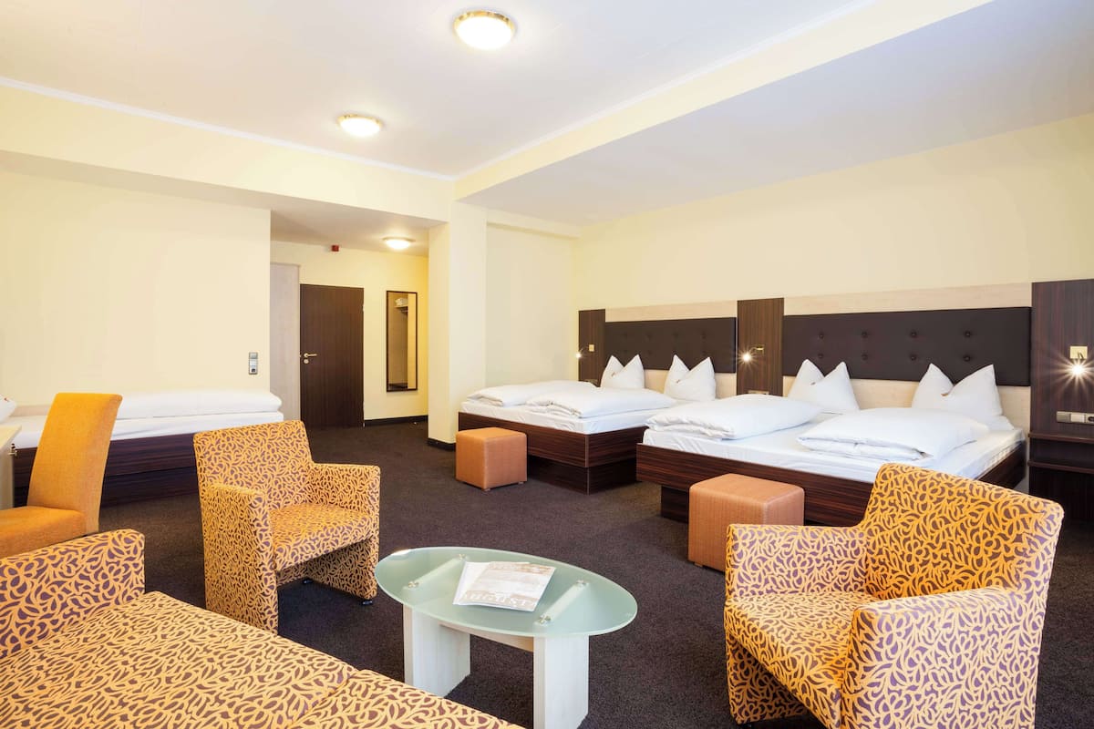 Ein Hotelzimmer mit zwei Betten, einem Schlafsofa, einem Sessel und einem kleinen Tisch.