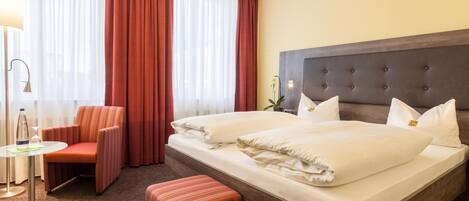 A hotel room with a bed, a chair, a table, and a lamp.