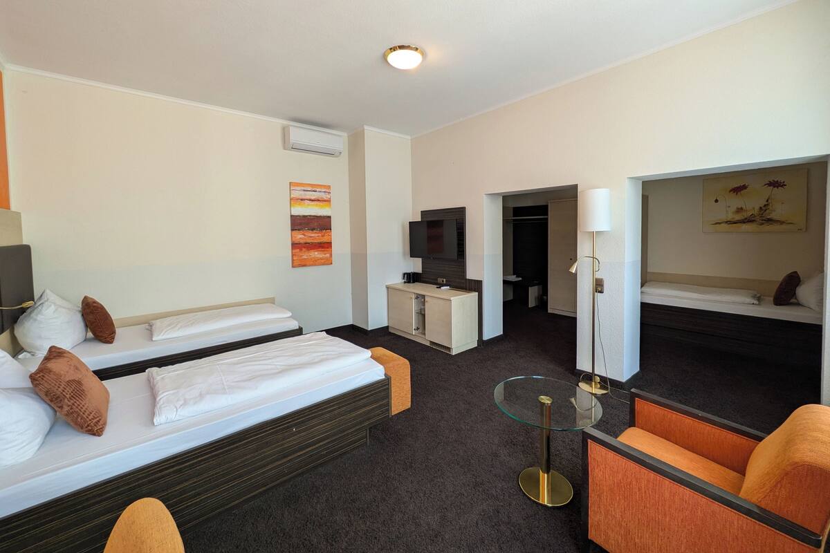 Ein Hotelzimmer mit zwei Betten, einem Schreibtisch, einem Fernseher, einem Glastisch und einem Sessel.